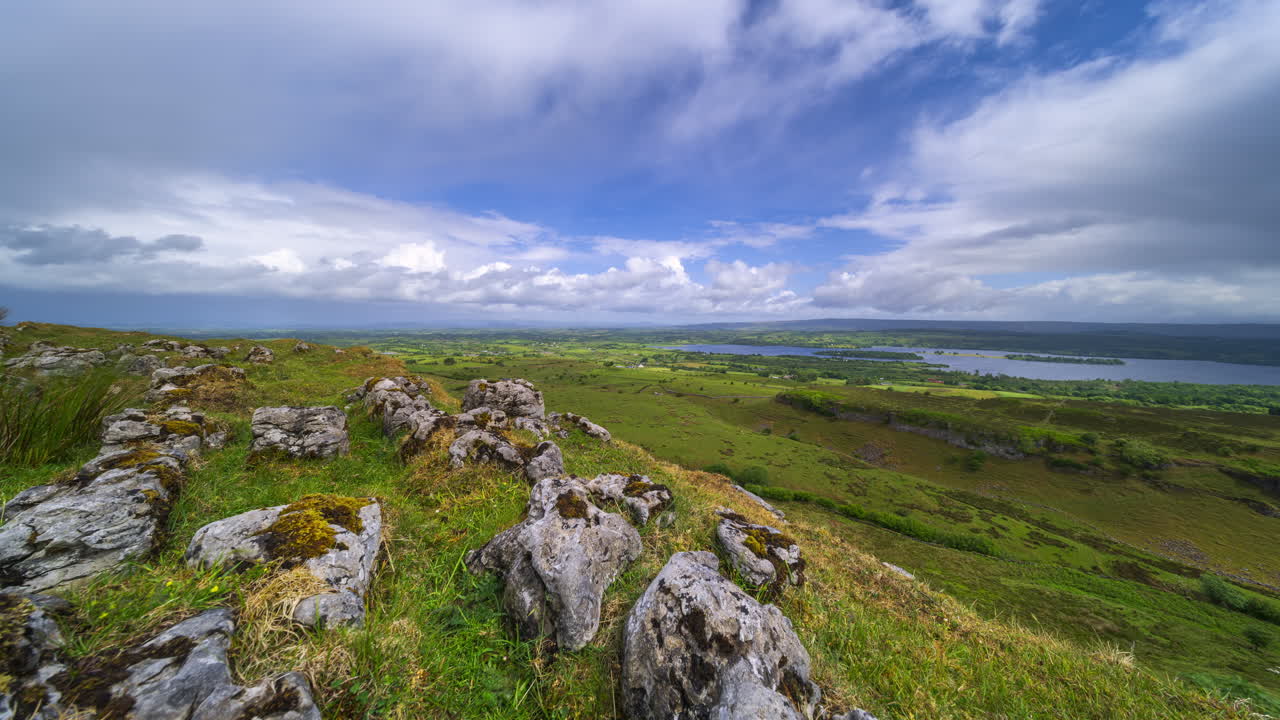 Tidsforløb af landligt landskab med klippeformation i forgrunden og bakker samt sø i det fjerne under en dag med forbipasserende regnvejr set fra Carrowkeel i Sligo County i Irland