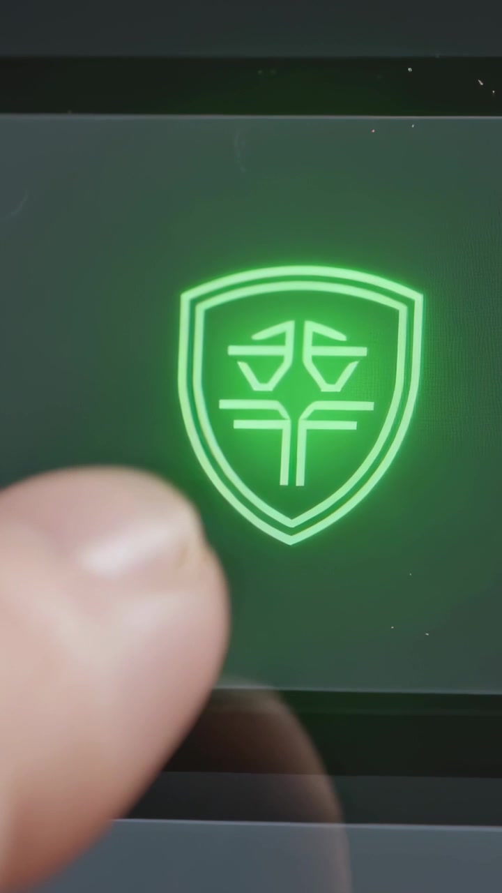 Video verticale: Pollice dell'utente che tocca e attiva l'emblema dello scudo su uno schermo portatile, mostrando un bagliore verde.