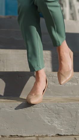 piernas femeninas con zapatos de tacón alto caminan por las escaleras de la casa a la calle en un día cálido. mujer en traje de pantalón verde camina por el pavimento en una gran ciudad de primer plano