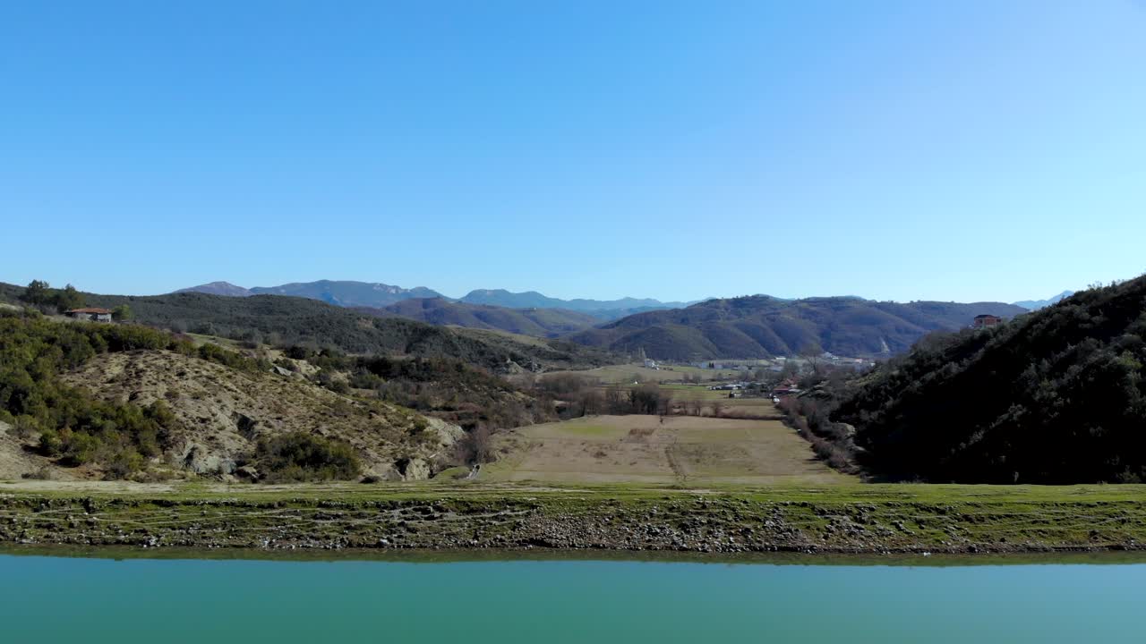 tranquila superficie de agua cristalina del embalse con presa sobre campos agrícolas y casas de pueblo en un hermoso valle rodeado de montañas, cielo azul claro