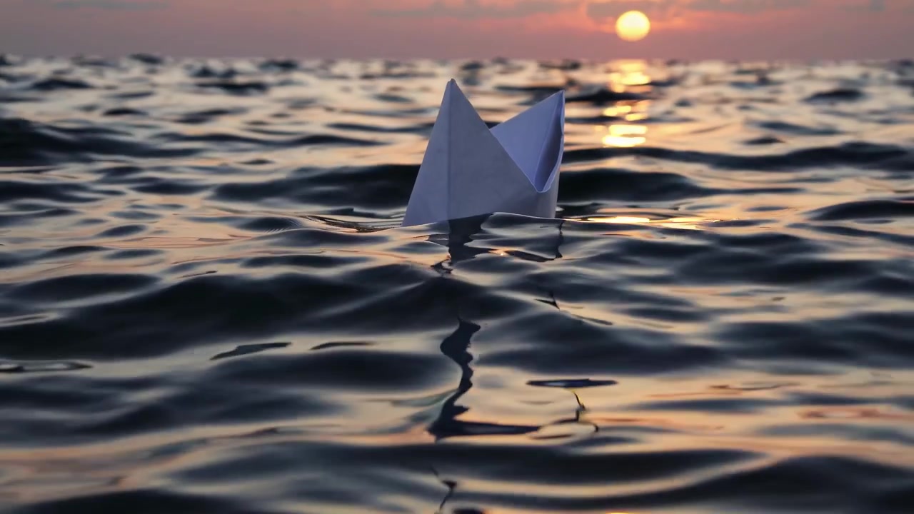 Small Paper Boat Floating on Calm Ocean Waves at Sunset