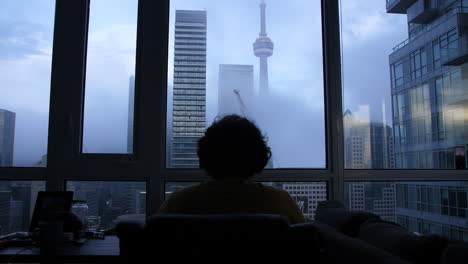 a man working at his apartment desk overlooking the toronto cn tower