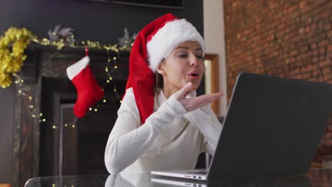 Frau-Mit-Weihnachtsmütze-Wirft-Einen-Kuss-Zu,-Während-Sie-Zu-Hause-Einen-Video-Chat-Auf-Dem-Laptop-Führt