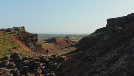 Aerial-view-of-man-explorer-backpacker-running-hiking-a-rock-formation-in-Iceland.-Drone-view-of-young-man-tourist-discovering-amazing-wilderness-of-desert-panorama-with-stone-cliff