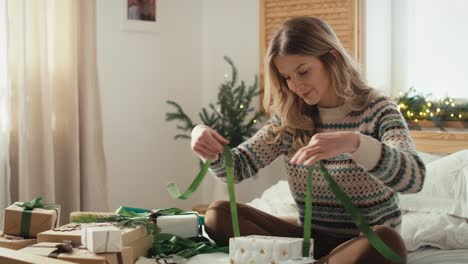 Focus-caucasian-woman-sitting-on-bed-and-packing-Christmas-gift-at-home