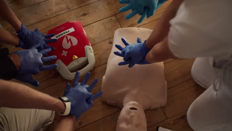 disparo de primer plano: una enfermera profesional con un uniforme blanco enseña a un grupo de personas con guantes médicos azules cómo doblar las manos en primeros auxilios y ejerce presión sobre un maniquí. una clase médica práctica