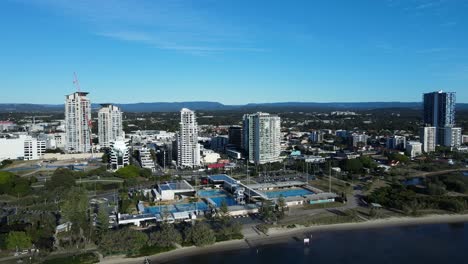 Hochschwenkender-Blick-Auf-Ein-Großes-Wassersportzentrum-An-Einer-Küstenwasserstraße-Mit-Einer-Hoch-Aufragenden-Städtischen-Skyline-Im-Hintergrund