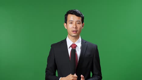 asian male tv news reporter in formal wear talking on a green screen, chroma key