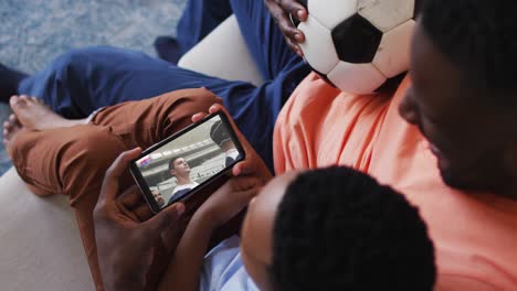 composite of father and son at home watching rugby match on smartphone