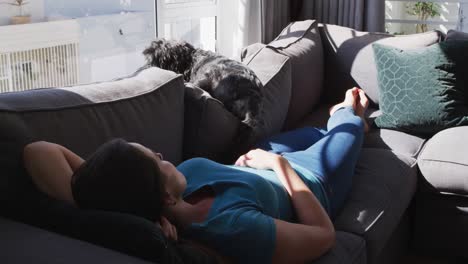 Caucasian-woman-lying-on-couch-with-dog-taking-a-nap