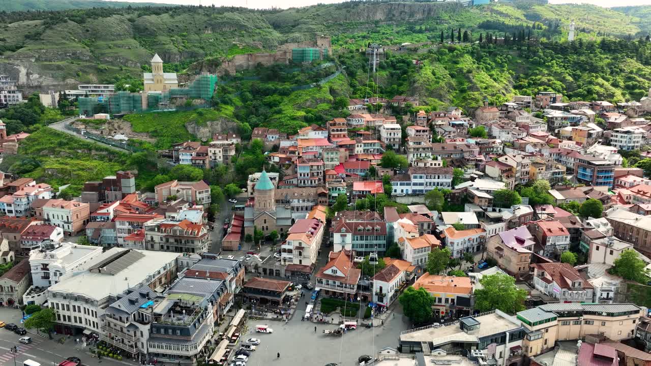 A charming drone capture of Tbilisi’s old quarter filled with colorful houses, narrow streets, and historic churches surrounded by green hills