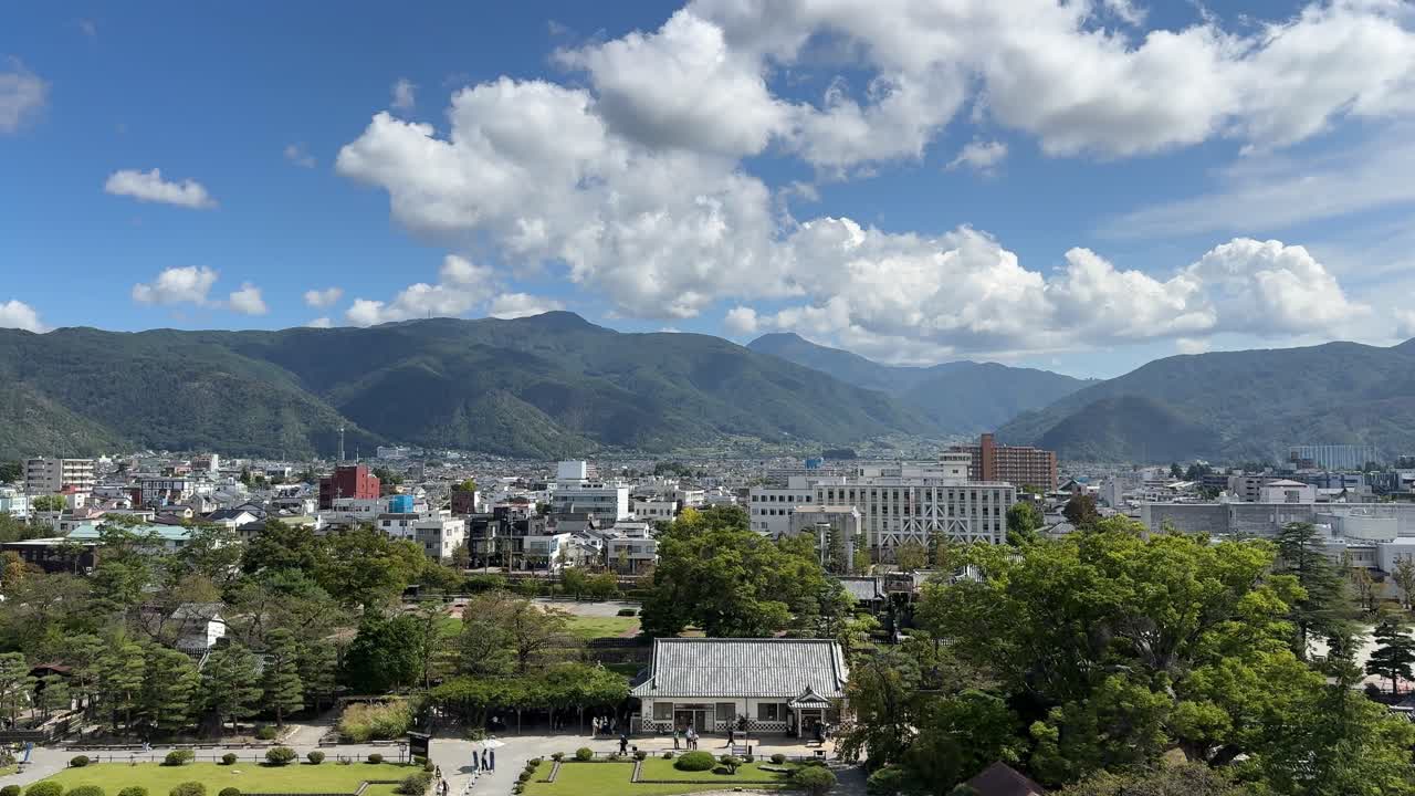 Ammira una vista panoramica mozzafiato dal castello di Matsumoto, che cattura il vivace fogliame autunnale, le maestose montagne e la vivace città sotto un cielo azzurro.