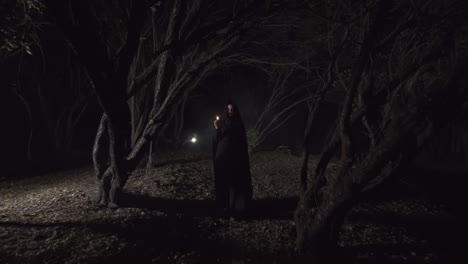 chica mística en un bosque oscuro con una vela en un manto oscuro