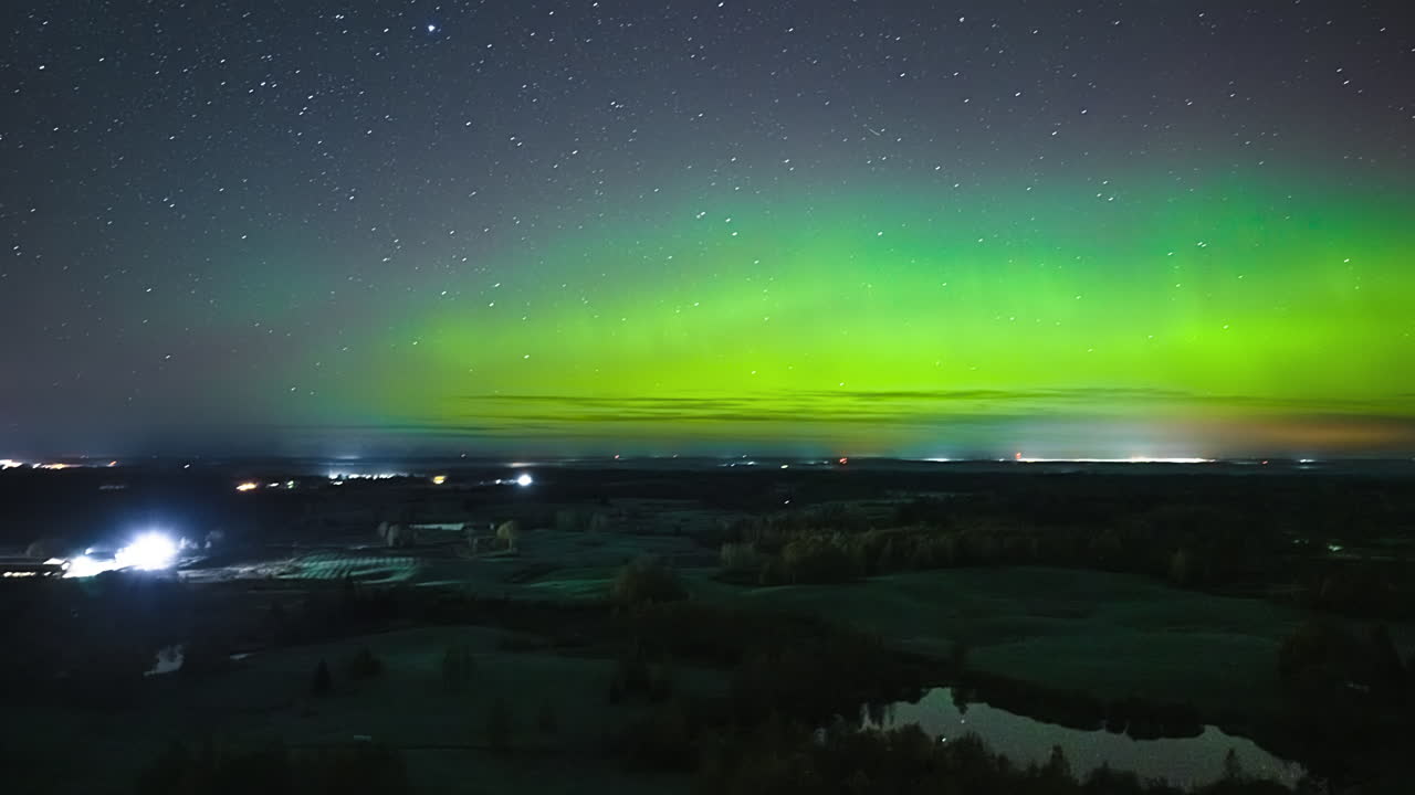 Aerial time-lapse of Aurora borealis waves and stars above countryside fields