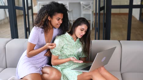 dos mujeres jóvenes usando una computadora portátil juntas en un sofá