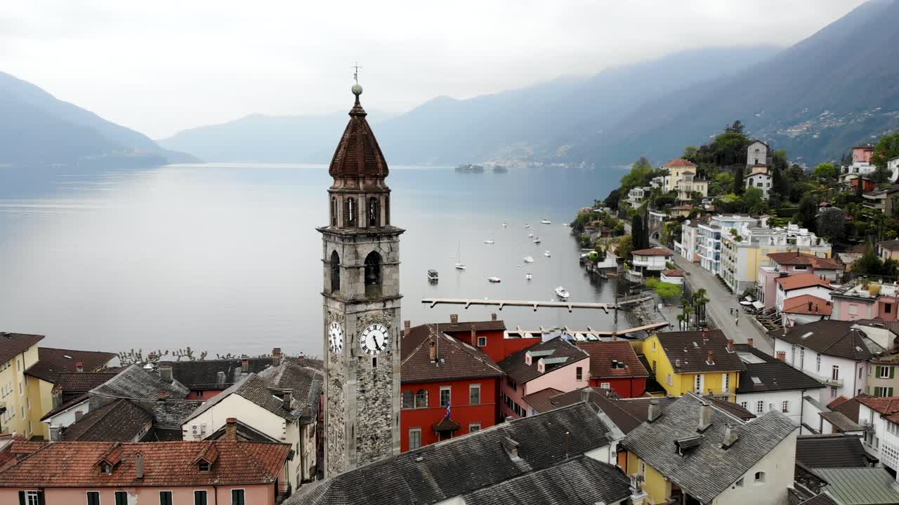 sobrevuelo aéreo alrededor de la torre del campanario de la iglesia chiesa dei santi pietro e paolo y sobre los tejados ascona, suiza, revelando las aguas del lago maggiore y los alpes en el fondo