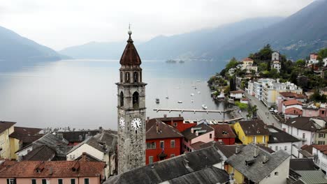 aerial flyover around the belfry tower of the chiesa dei santi pietro e paolo church and over the rooftops ascona, switzerland revealing the waters of lago maggiore and alps in the background