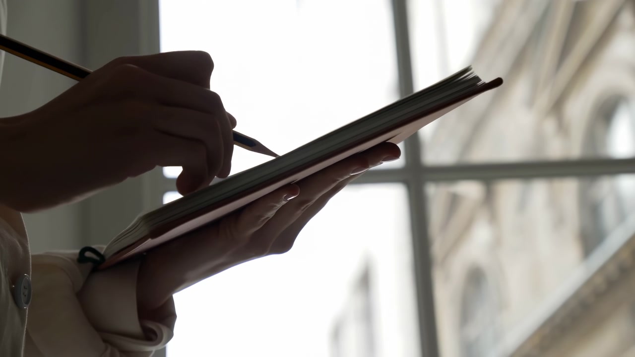 Close view of an adult hand holding a pen and filling out a clipboard beside a sunlit window, with strong backlight, dark silhouettes, and a quiet indoor