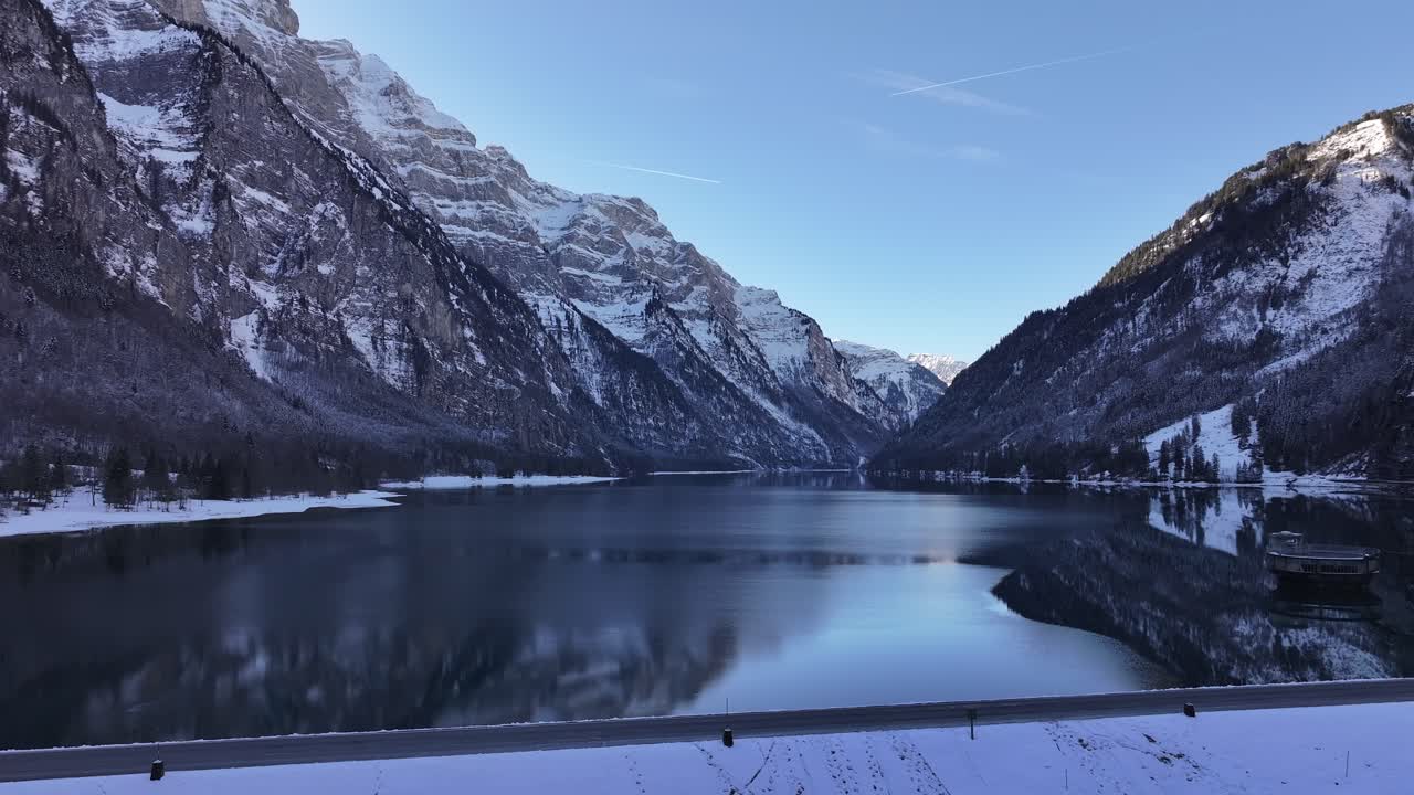 Snow covered dam with Klöntalersee reflecting snowy Alps in Klöntal, Switzerland