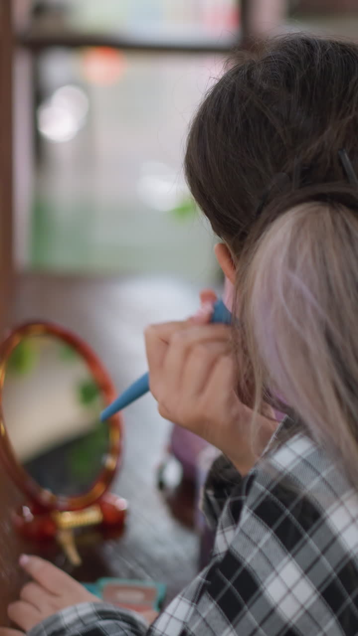 niña joven frente al espejo del tocador practicando la técnica del pincel, luz de fondo suave de la ventana, camisa de cuadros y coleta con reflejos de luz, pincel suave acariciando las mejillas, polvera y maquillaje sobre la mesa, espejo redondo