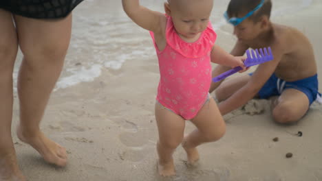 a baby girl in a pink swimsuit on a beach with her mother