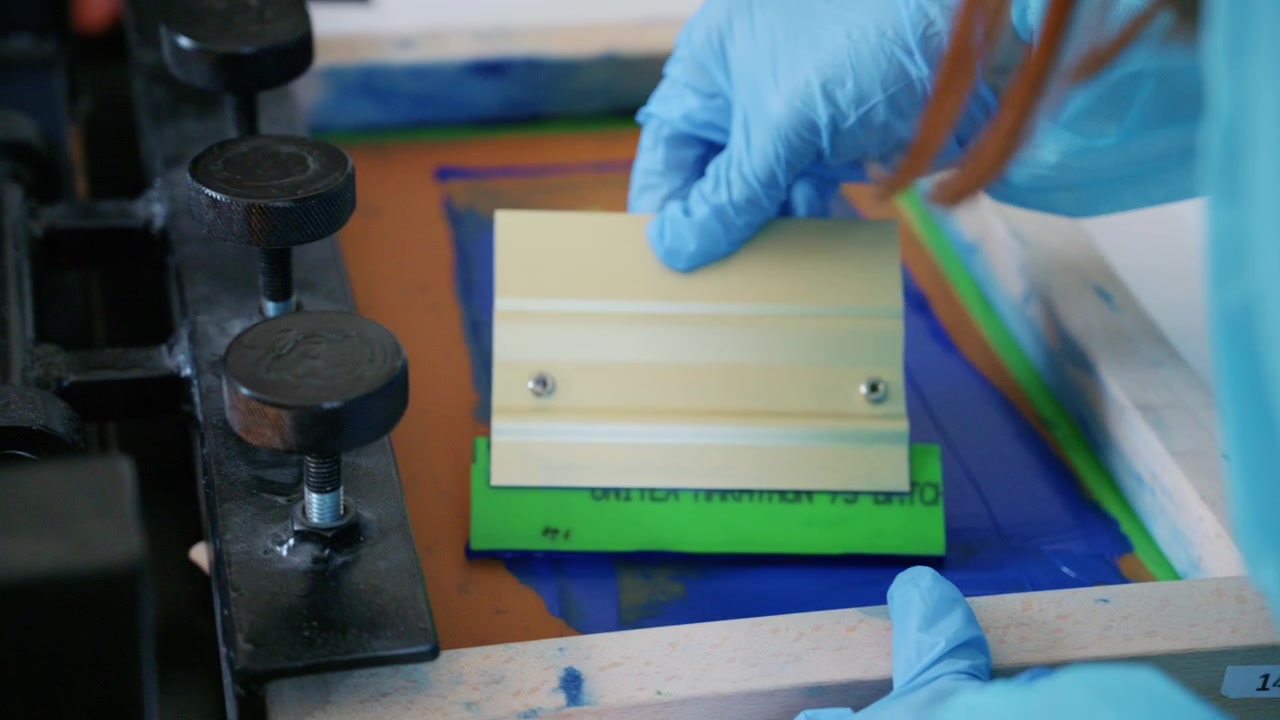 Worker using a squeegee to spread ink across a screen printing frame during textile production