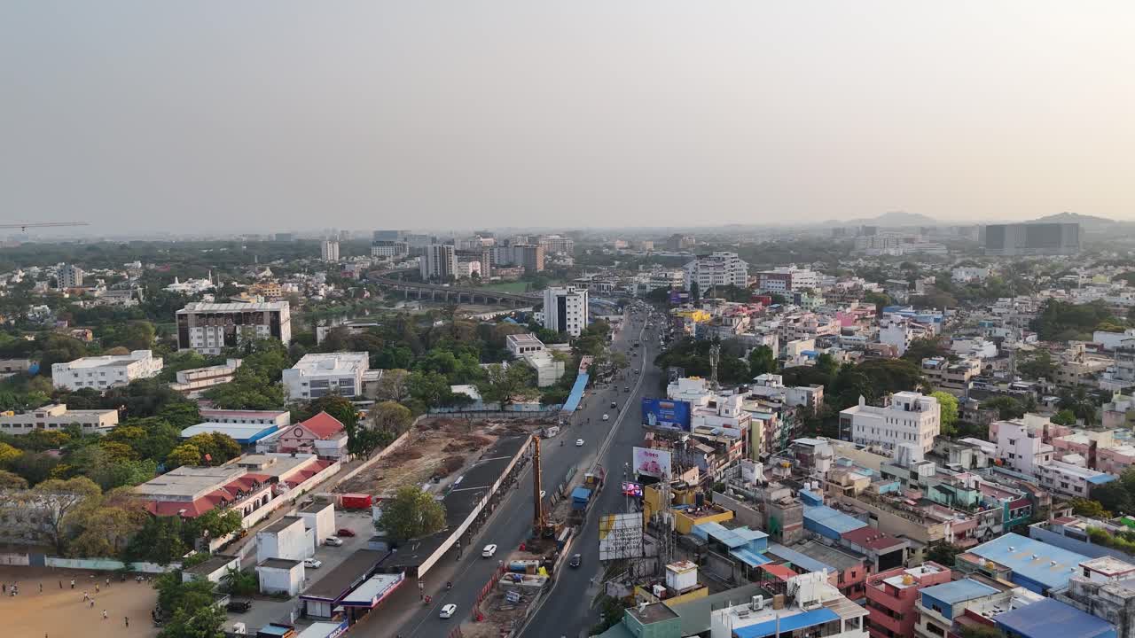 Aerial view Chennai's Little Mount, Saidapet. Anna Salai, divides the scene. In the foreground, a large field with people, while new high-rise construction dominates the left. The Saidapet Bridge