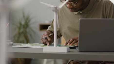 businessman using laptop sitting at table with windmill model in the office