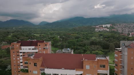 Close-aerial-flyover-of-apartment-buildings-revealing-a-pond-and-mountains-in-Cali,-Colombia