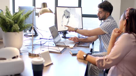 discussing robot design, colleagues collaborating at desk with laptop and monitor