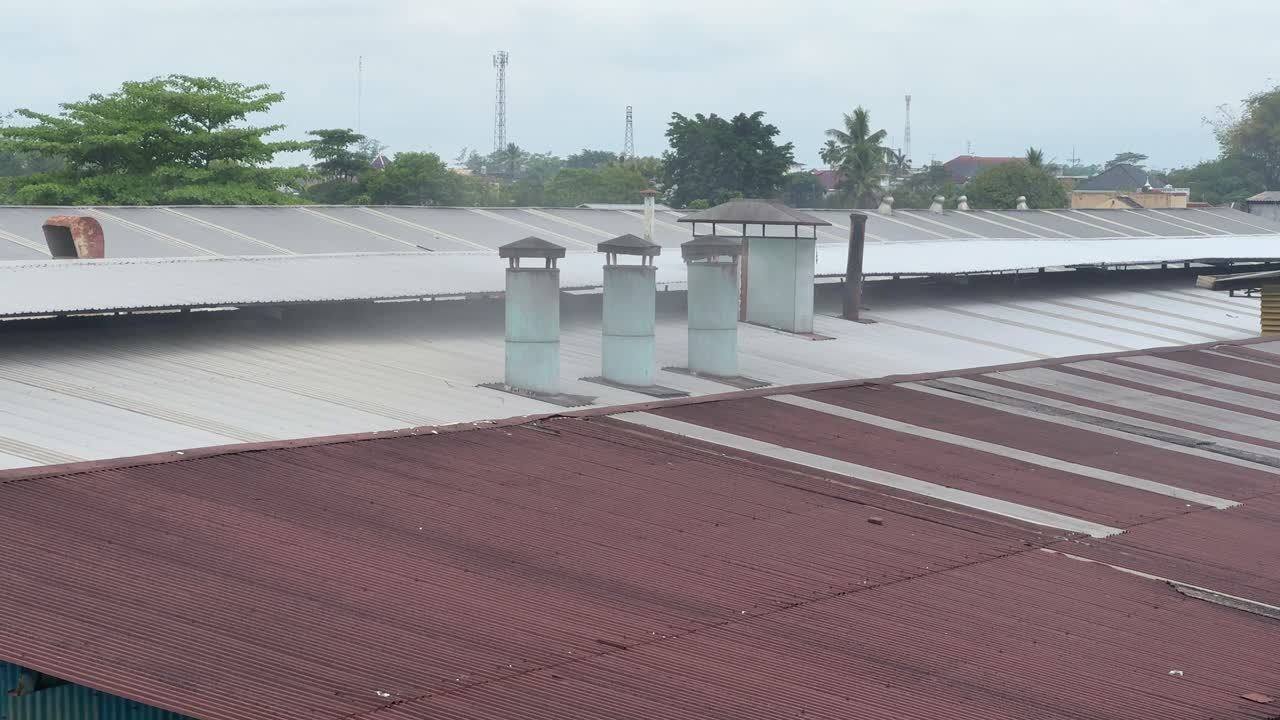 Industrial chimneys releasing light smoke above a large factory rooftop. Movement of emissions as they drift across the metal roof. Manufacturing, industry, pollution, and environmental impact