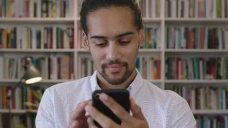 close up portrait of young hispanic man student enjoying texting browsing online using smartphone mobile app in library bookshelf background research learning