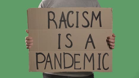 a man holds in front of him a poster from a cardboard box with the words racism is a pandemic. isolated a green screen, chroma key. close up. slow motion