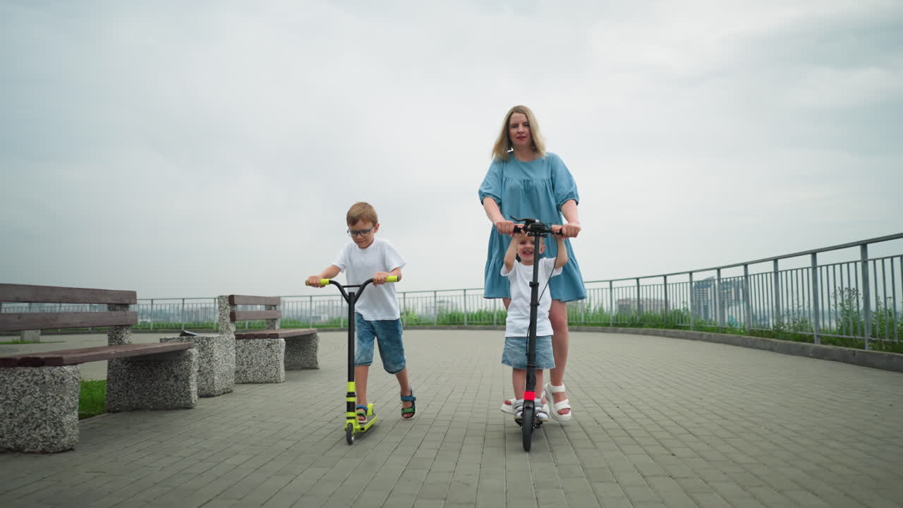 A mother and her children are riding scooters along a curved pathway, the younger child is with his mum, while the older child rides independently