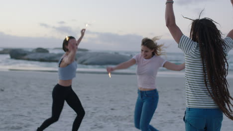 Fröhliche-Gruppe-Von-Freunden,-Die-Licht-Wunderkerzen-Tanzen-Und-Am-Silvester-Sonnenuntergang-Am-Strand-Feiern