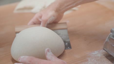 pov of baker making perfectly round bread loaf with dough scraper