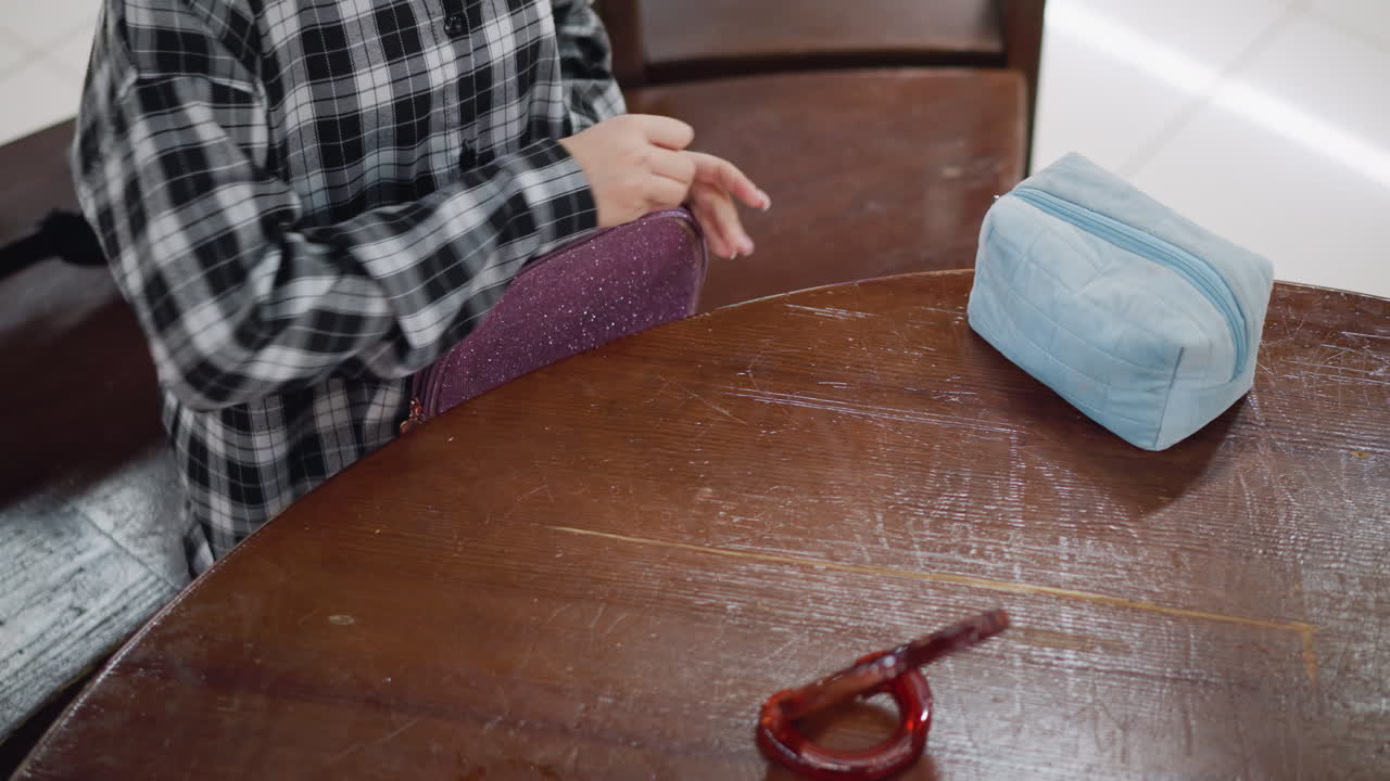 Closeup view of cosmetic artist in plaid shirt arranging makeup tools on wooden table, blue cosmetic bag and wooden mirror are placed on table as she organizes beauty essentials with precision