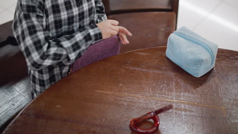 vista de cerca de la artista cosmética en camisa a cuadros organizando herramientas de maquillaje en una mesa de madera, bolsa de cosméticos azul y espejo de madera se colocan en la mesa mientras organiza los elementos esenciales de belleza con precisión