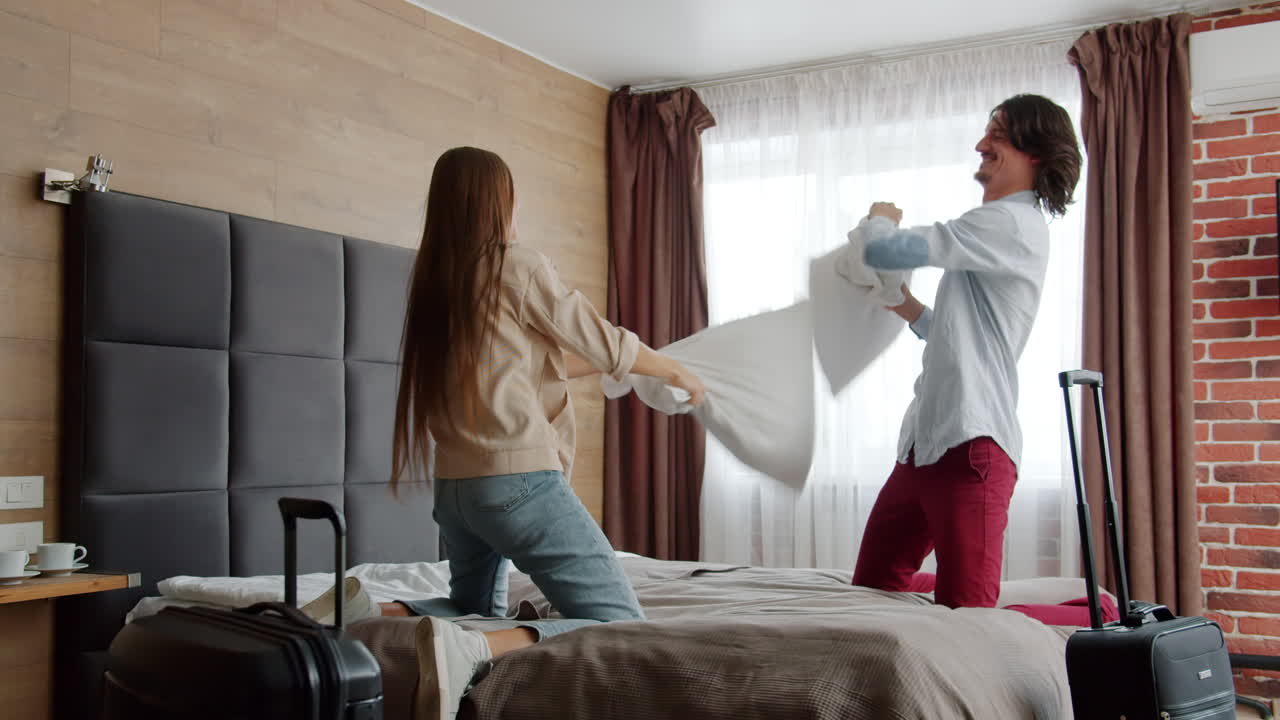 pareja teniendo una pelea de almohadas en una habitación de hotel