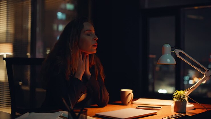 Lavoratore stanco si tocca la fronte, con le ore rimanenti da trascorrere in ufficio, primo piano