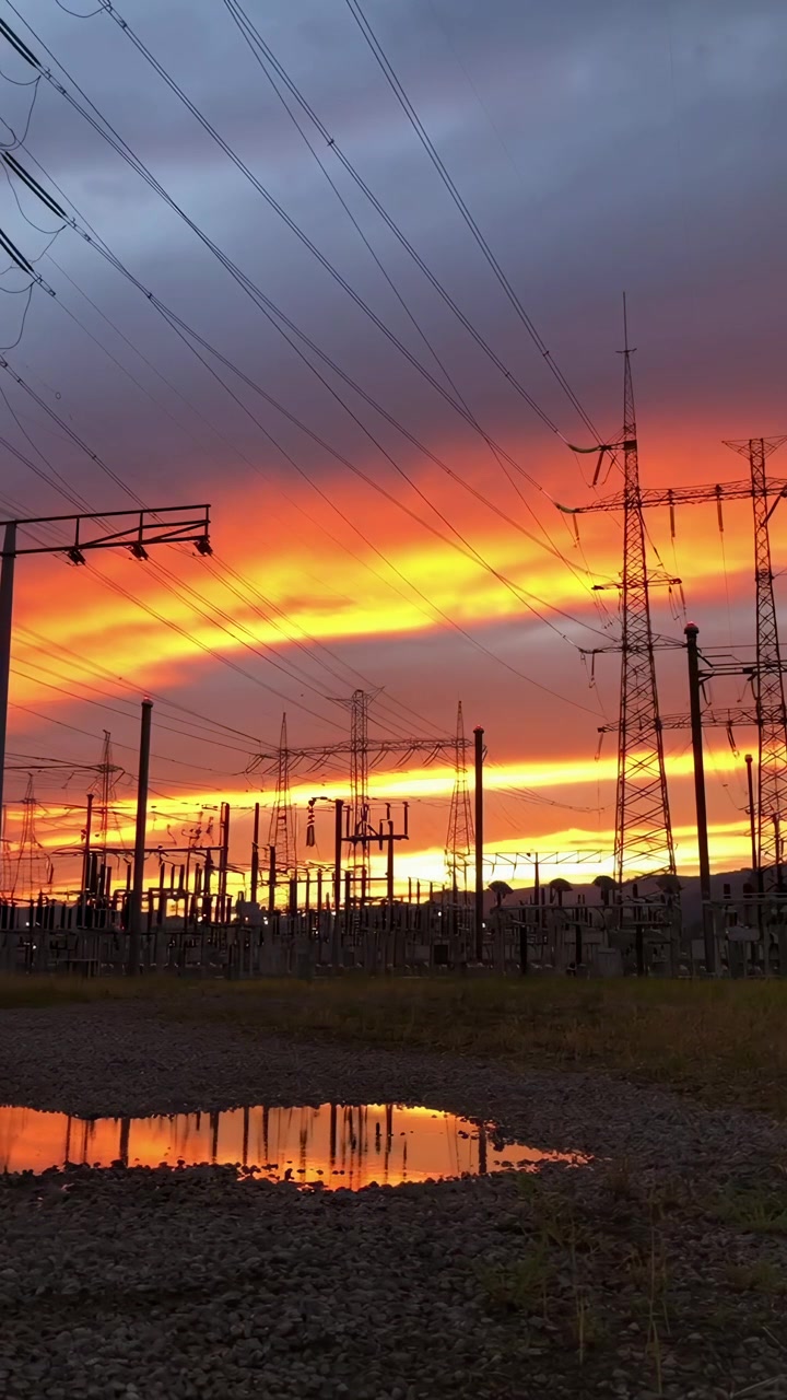 Céu dramático ao pôr do sol sobre uma subestação de energia com reflexo em poça.