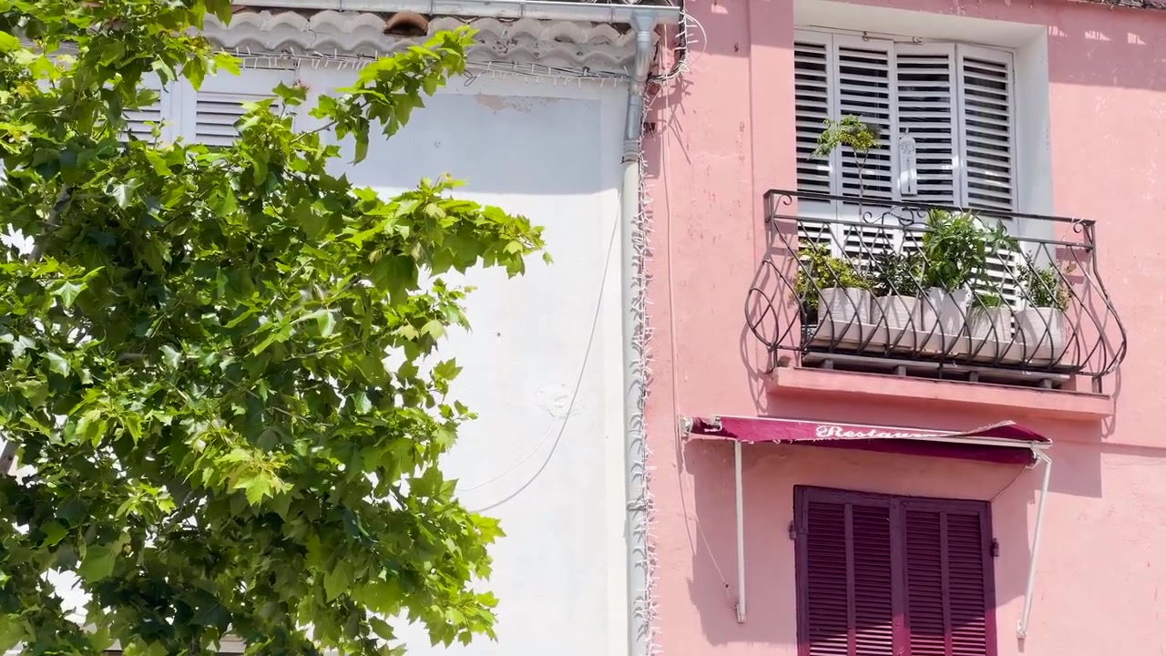 Ripresa statica di un edificio mediterraneo rosa con una tenda da sole di un ristorante e foglie verdi di alberi