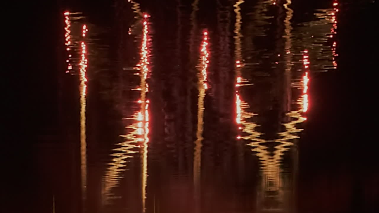 Comet fireworks reflected in water create abstract patterns in black