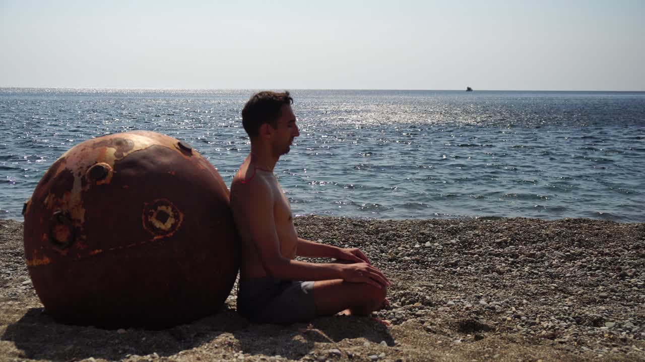 바가와 바다를 배경으로 해변에 오래된 녹은 떠다니는 해양 광산 근처에서 야외에서 요가 운동을 하는 남자 건강한 생활 방식, 오염, 자연 보호, 전쟁과 평화 개념