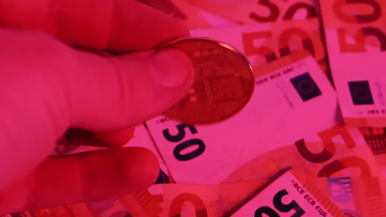 Bitcoin coin being held over scattered euro banknotes, digital and fiat currency