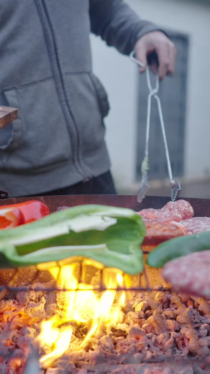 A person grilling meat and vegetables on a charcoal BBQ