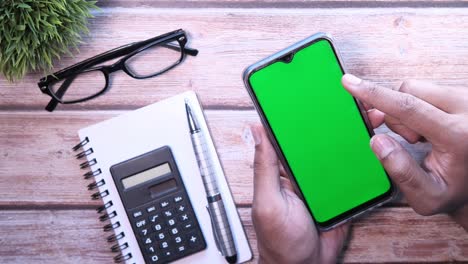 persona usando un teléfono inteligente con una pantalla verde, rodeada de suministros de oficina