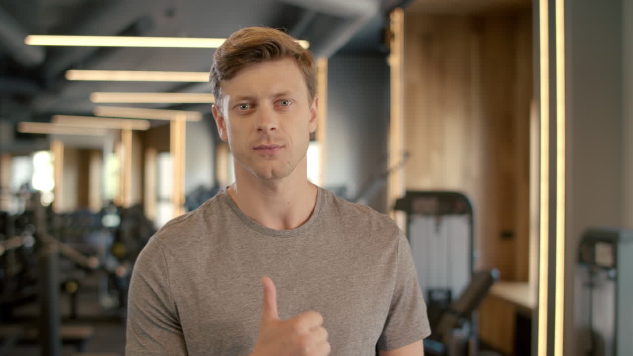 Uomo fitness serio che mostra il pollice in su in un club sportivo. Sportivo in piedi in palestra.