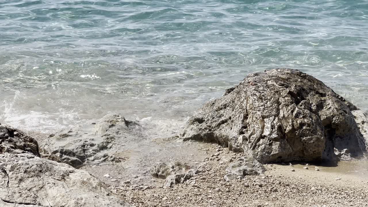Clear turquoise seawater gently washes onto a sandy, rocky beach in Croatia. The calm Adriatic scene highlights nature, travel, and a peaceful summer holiday atmosphere