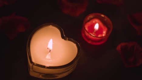 disparo de arriba de románticas velas rojas encendidas en forma de corazón en el fondo cubiertas de pétalos de rosa